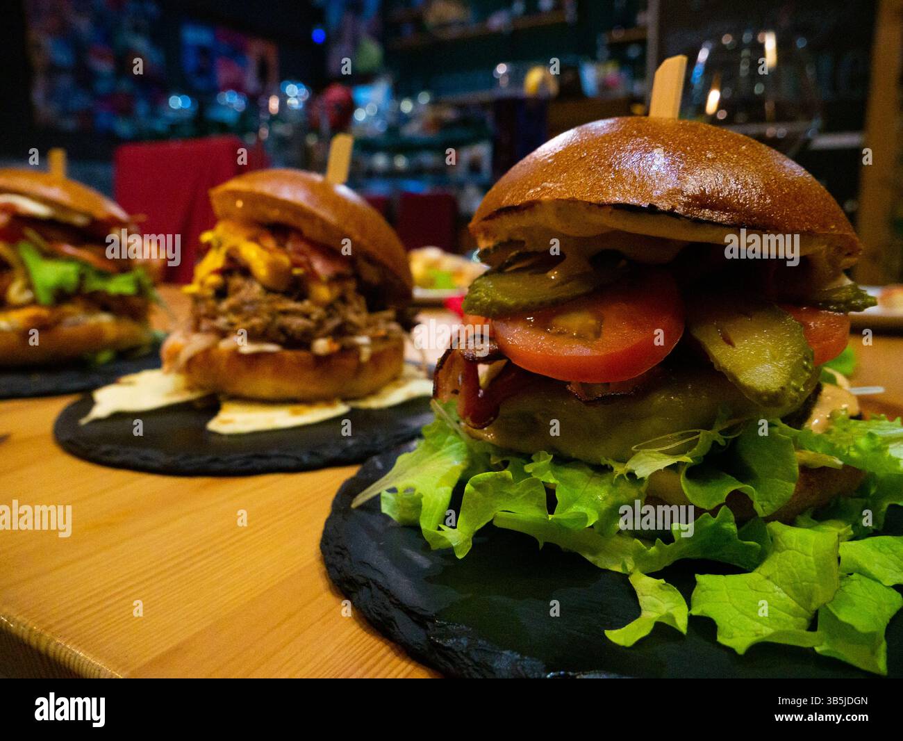 Three different gourmet burgers, each with unique toppings including meat, cheese, bacon, pulled pork, tomatoes, and pickles, are presented on black s Stock Photo