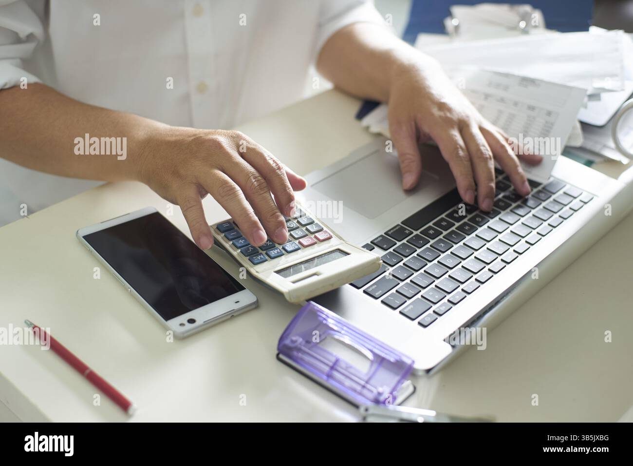 Geschaeftsmaenner arbeiten mit Taschenrechner und Laptop am weissen Tisch im Buero Stock Photo