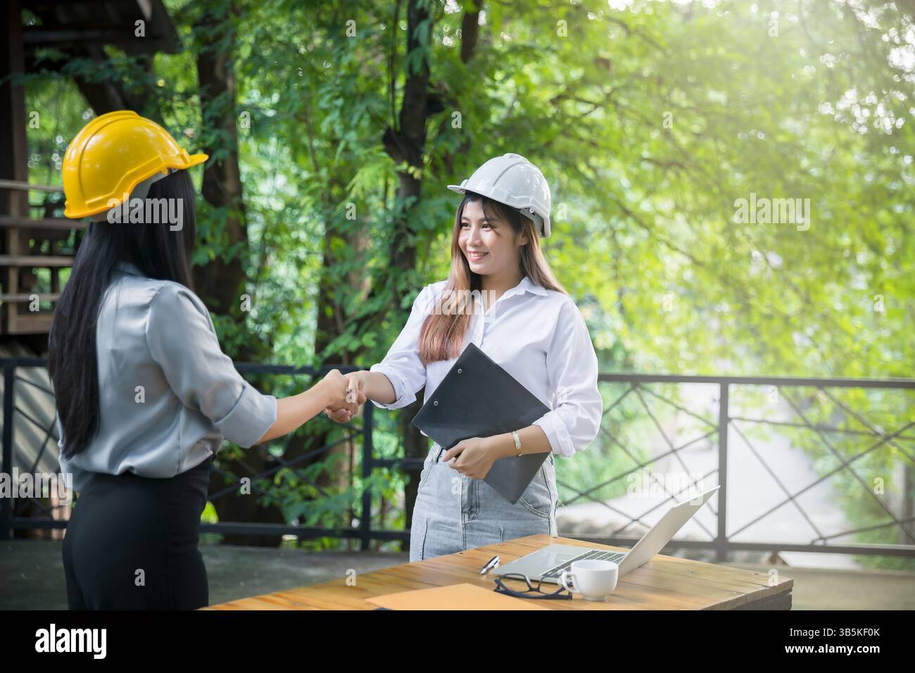 Two asian female architect and engineer in protective helmets shaking hands after meeting. Success collaboration concept. Stock Photo