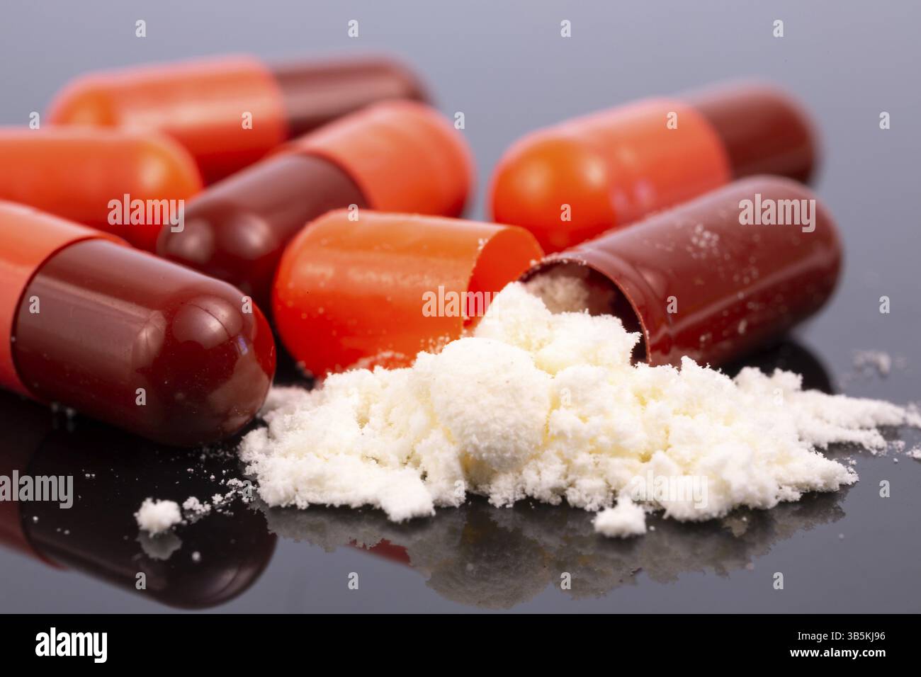 Some red capsules and white powder isolated on black reflective surface. Global pharmaceutical industry for billions dollars per year. Pharmaceutical Stock Photo