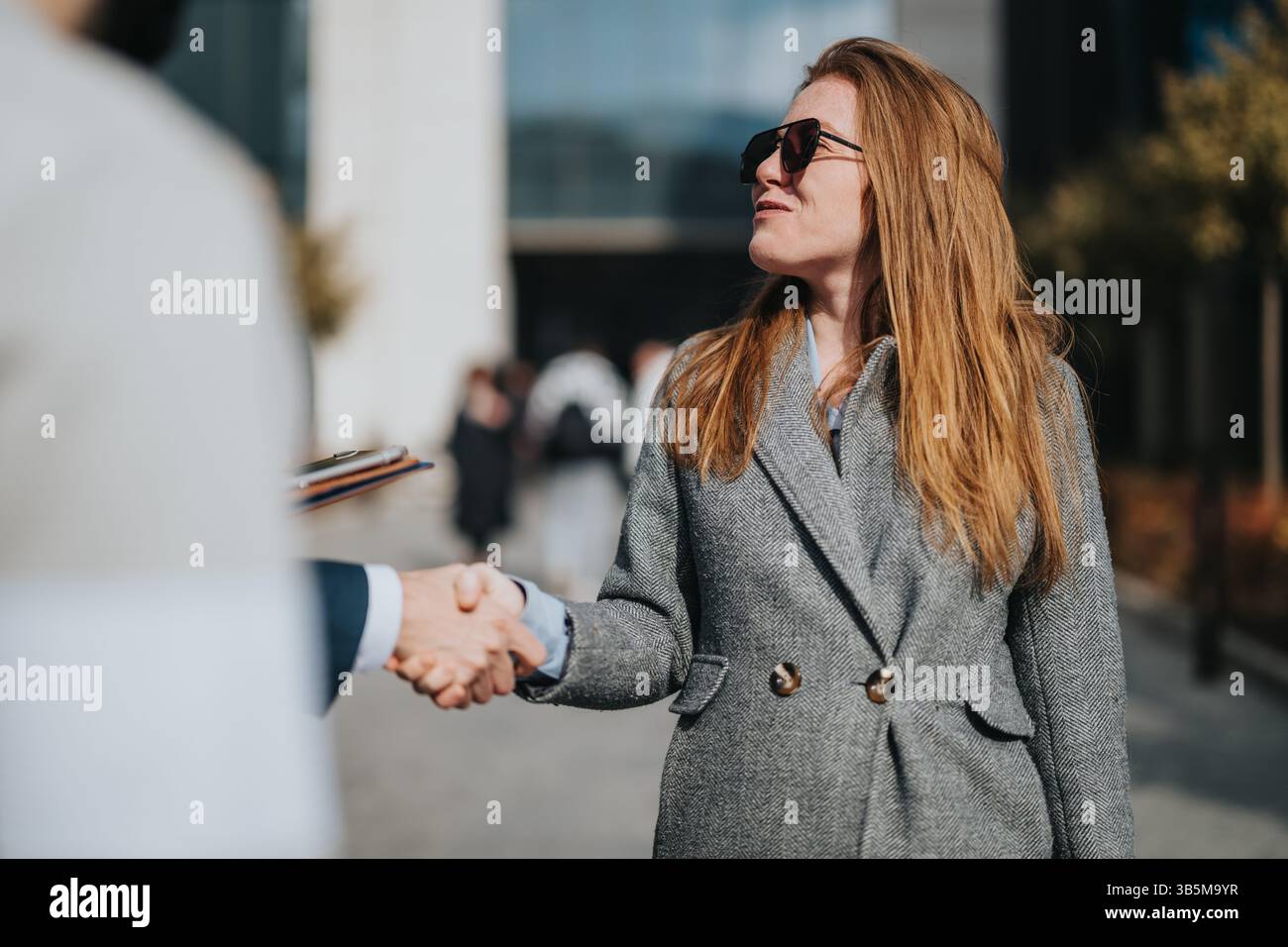 Professional handshake between two individuals outside a modern commercial building Stock Photo