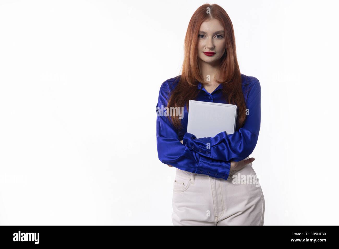 A confident woman in a blue blouse and white pants holding a clipboard, exuding professionalism and authority Stock Photo