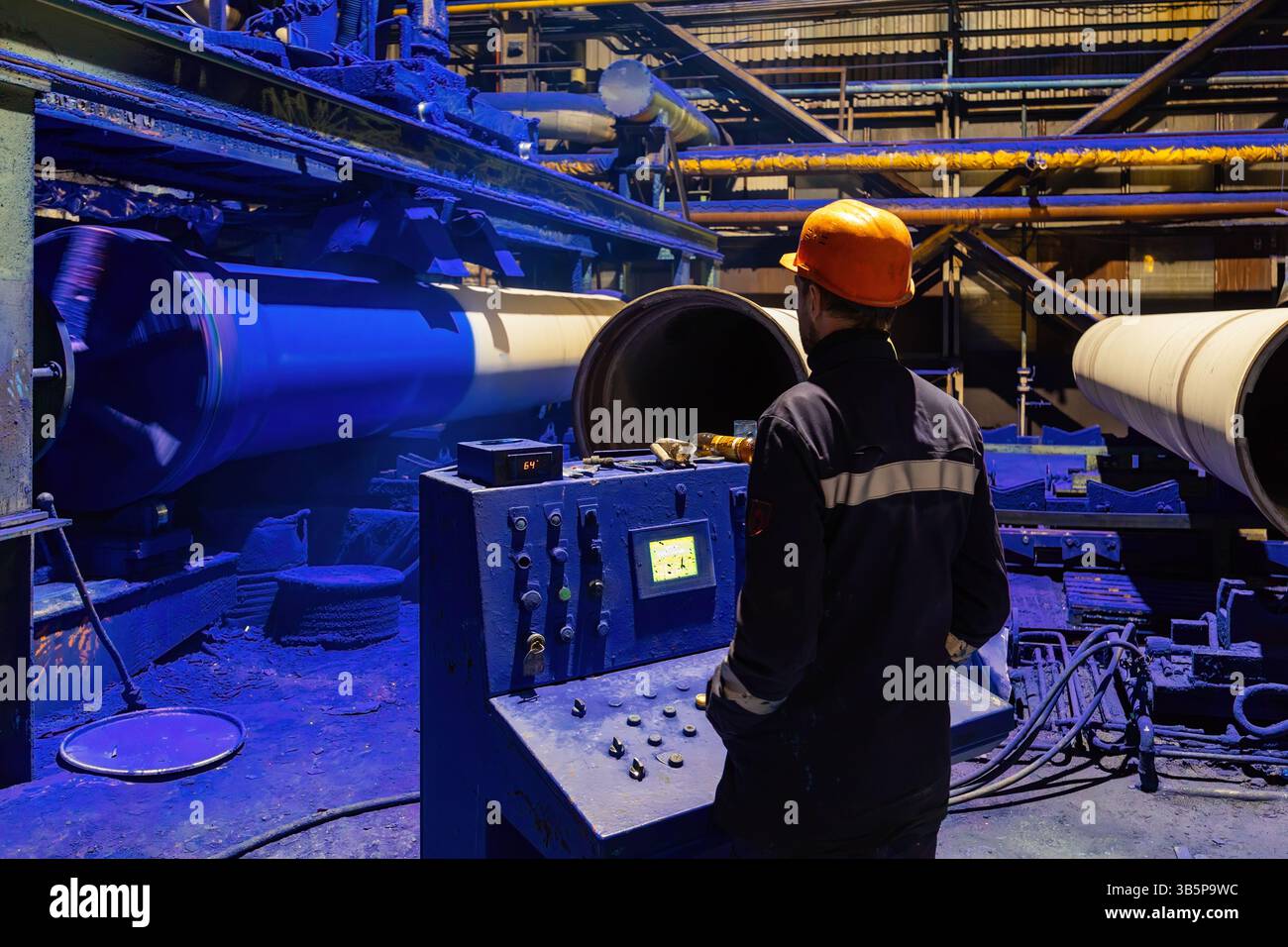 Factory engineer operates pipe painting automatic machine. Stock Photo