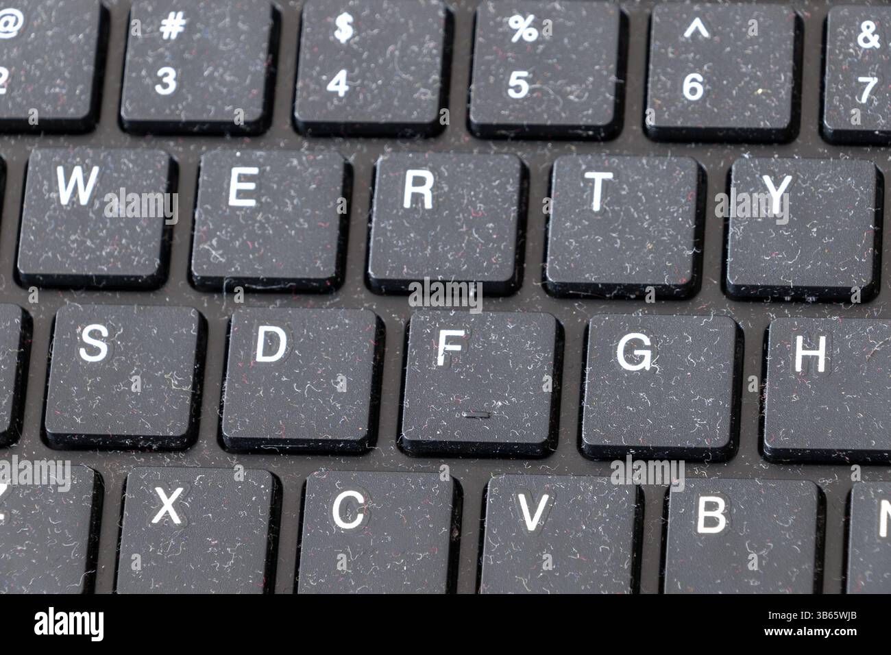 A close-up of a dusty black keyboard, with visible lint and debris accumulated between the keys. Stock Photo