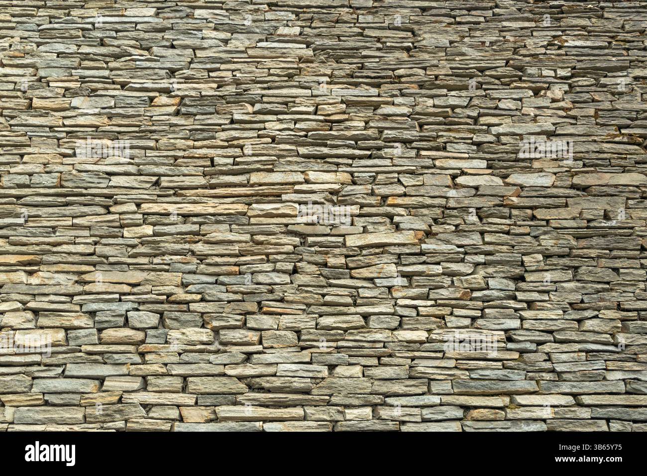 A tightly stacked stone wall with irregular, layered rocks, creating a rustic and textured pattern. Backgrounds Stock Photo
