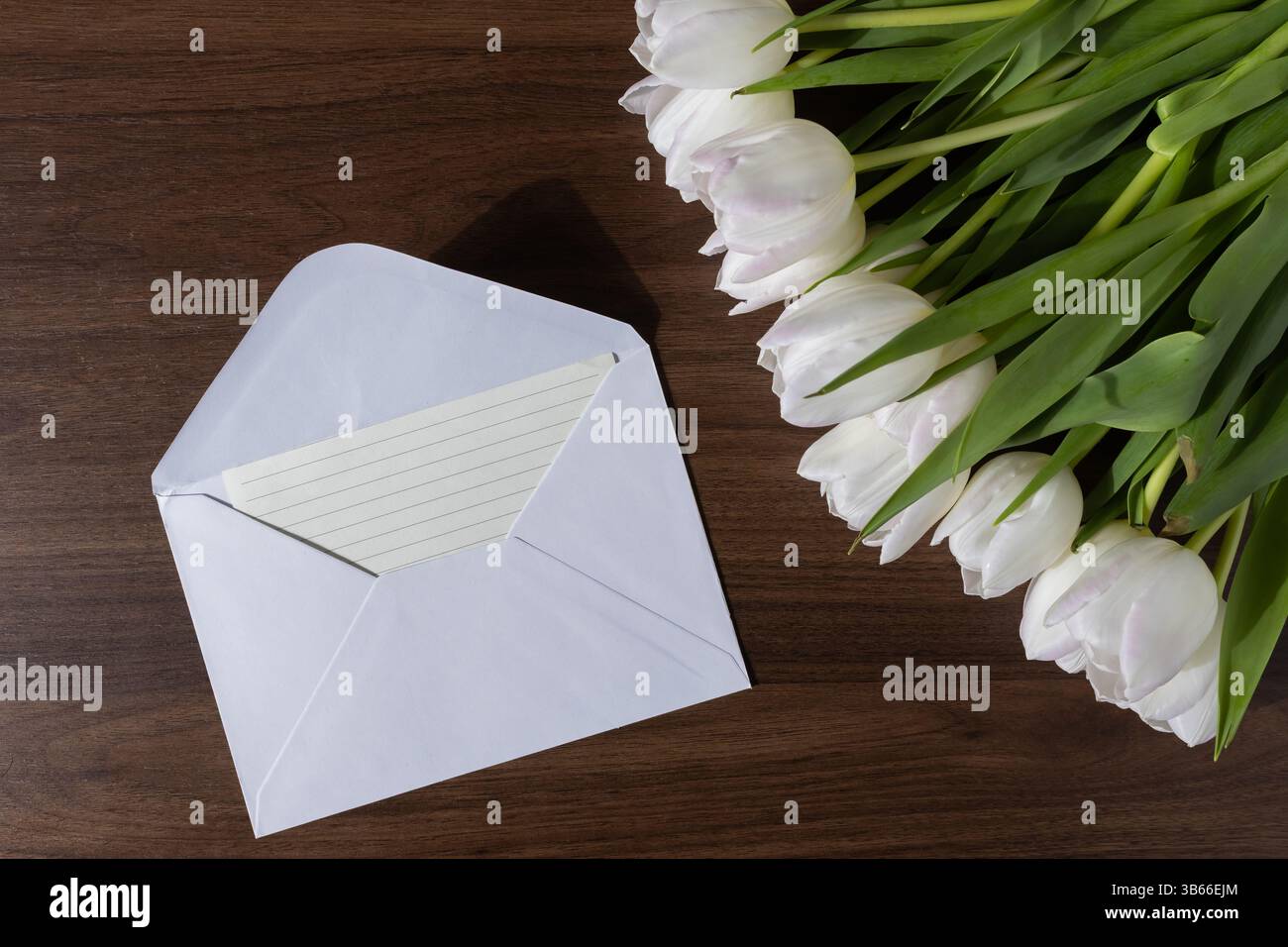 Overhead view of a white tulip arrangement with an open white envelope ...
