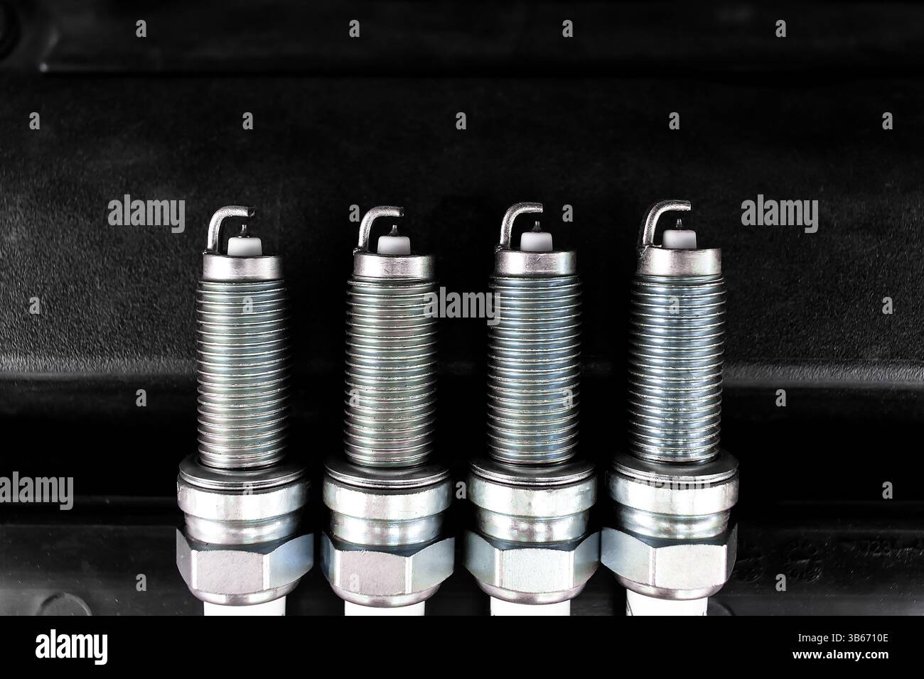 Car Spark Plugs, Close-up of four new iridium spark plugs are lined up against a dark background. DIY engine repair Stock Photo