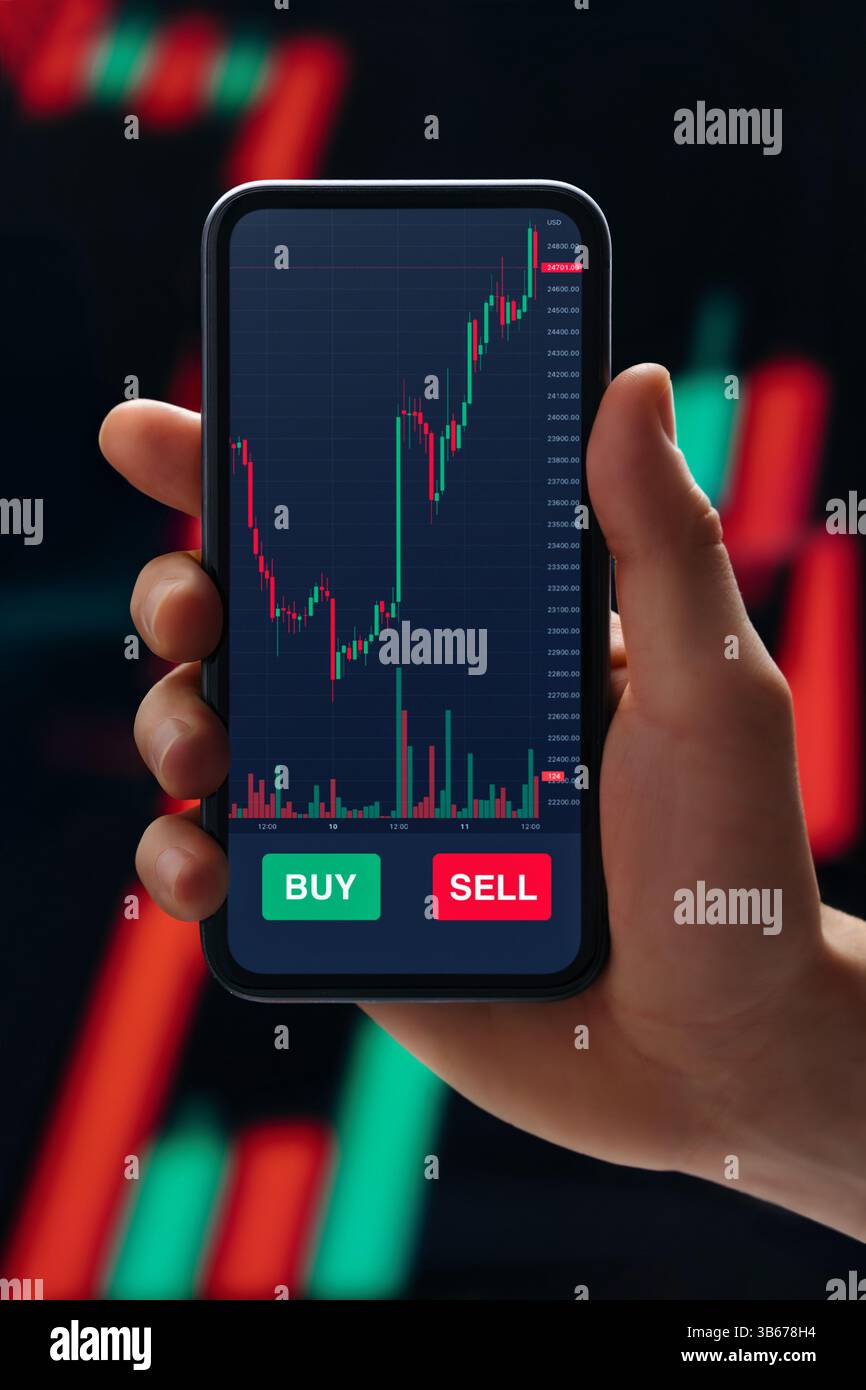 Close up, trader hand holding smartphone with stock market app on screen, against candlestick diagram on background. Online trading and investment concept Stock Photo