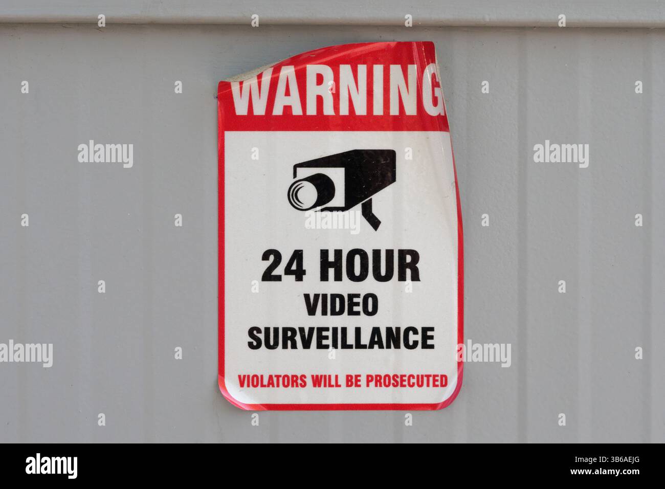 Peeling warning sign indicating 24 hour video surveillance is attached to a gray wall Stock Photo