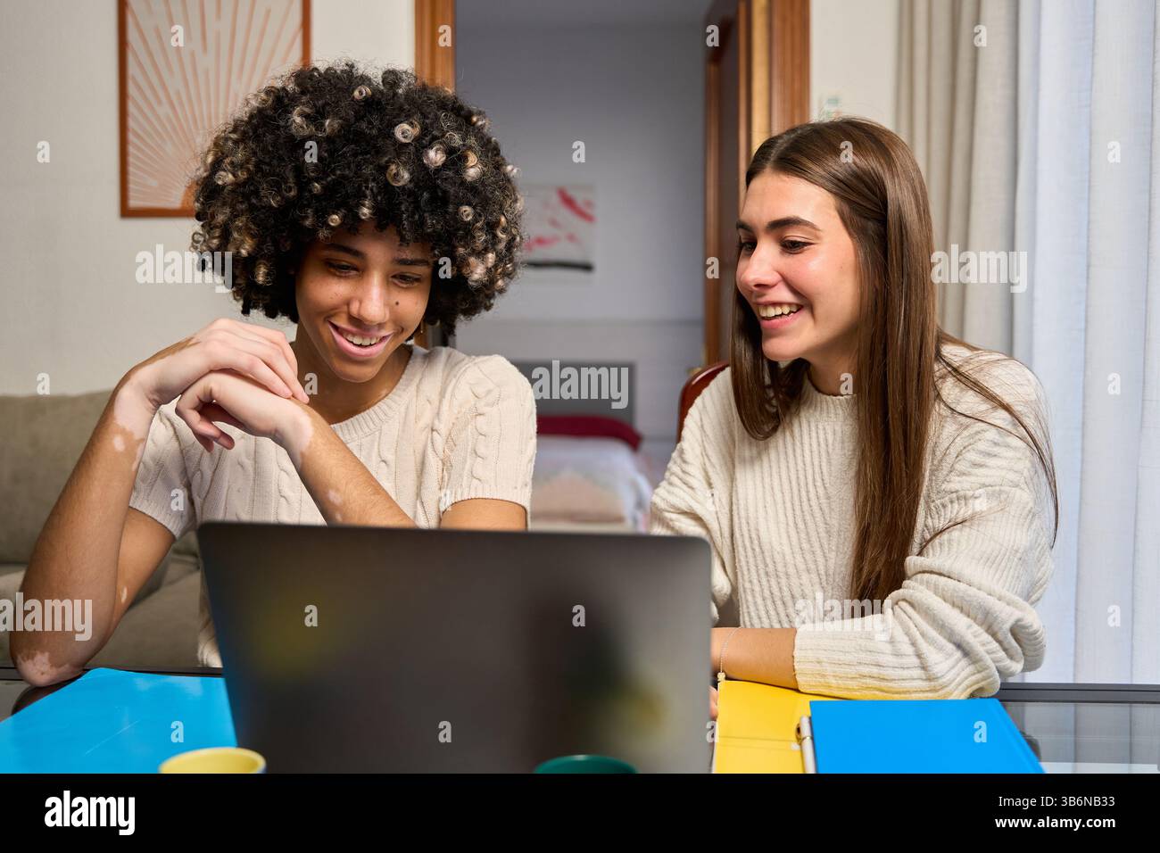 Two happy female students collaborating on laptop at home Stock Photo