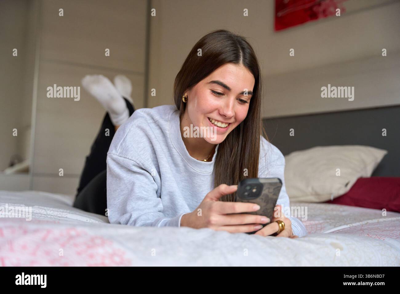 Happy female student using smartphone while lying on bed Stock Photo