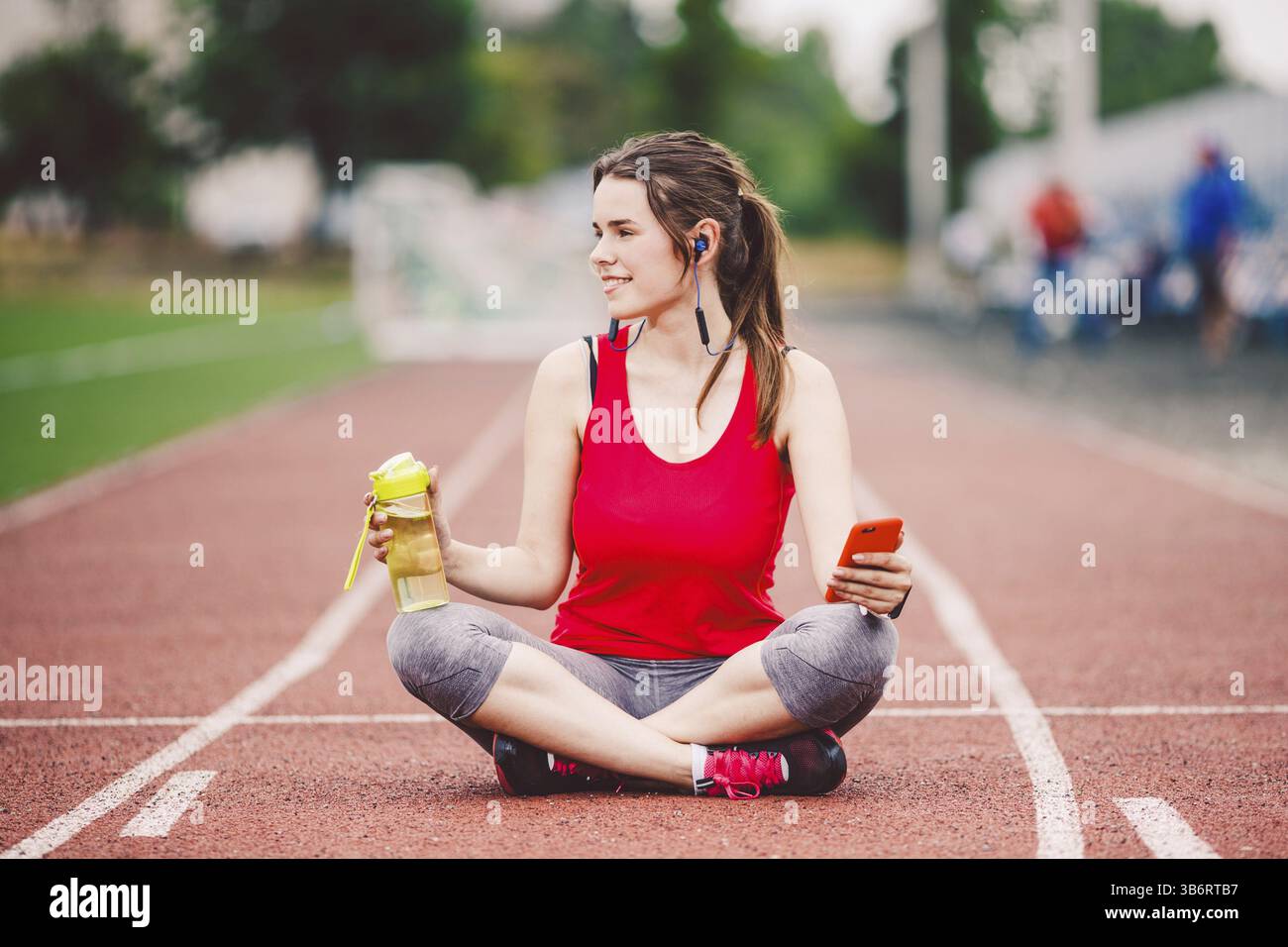 Beautiful fitness girl uses smartphone at stadium after workout. Sports and healthy. Sport woman use of cellphone inside sport complex. Sport and tech Stock Photo