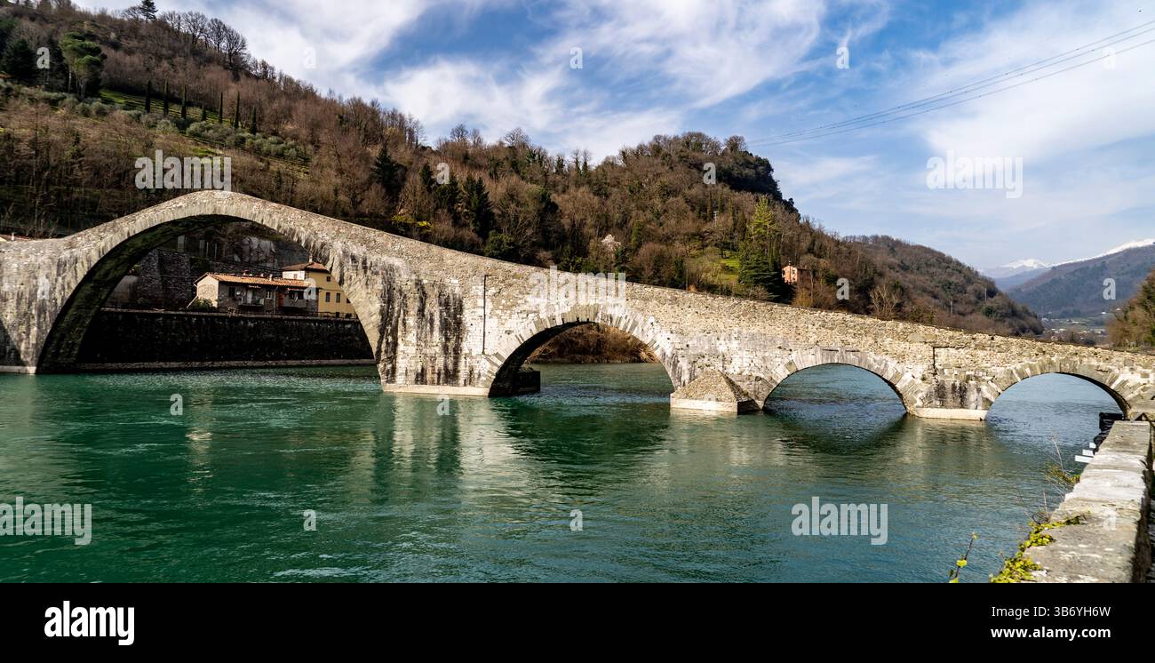 A historic stone bridge arches over a calm river, surrounded by lush ...