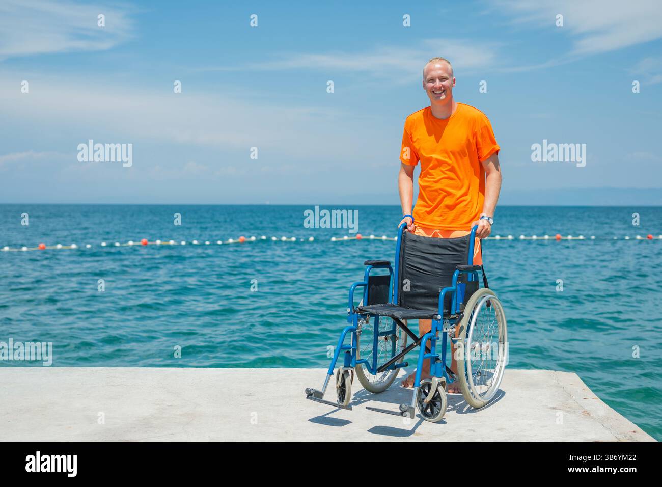Young smiling man, lifeguard at an accessible beach and assistant for ...