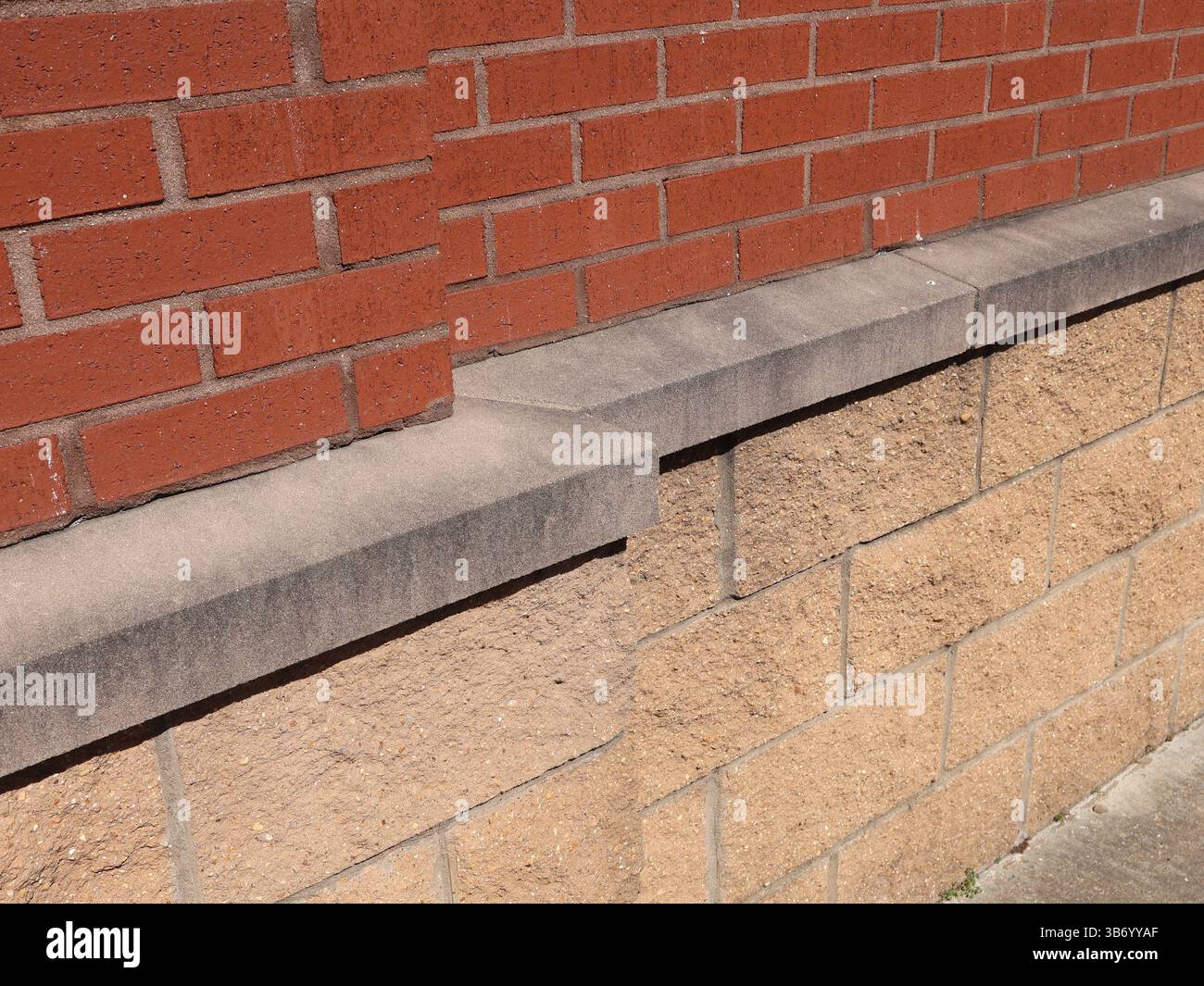 red brick traditional masonry pattern and concrete block wall separated by precast concrete ledge Stock Photo