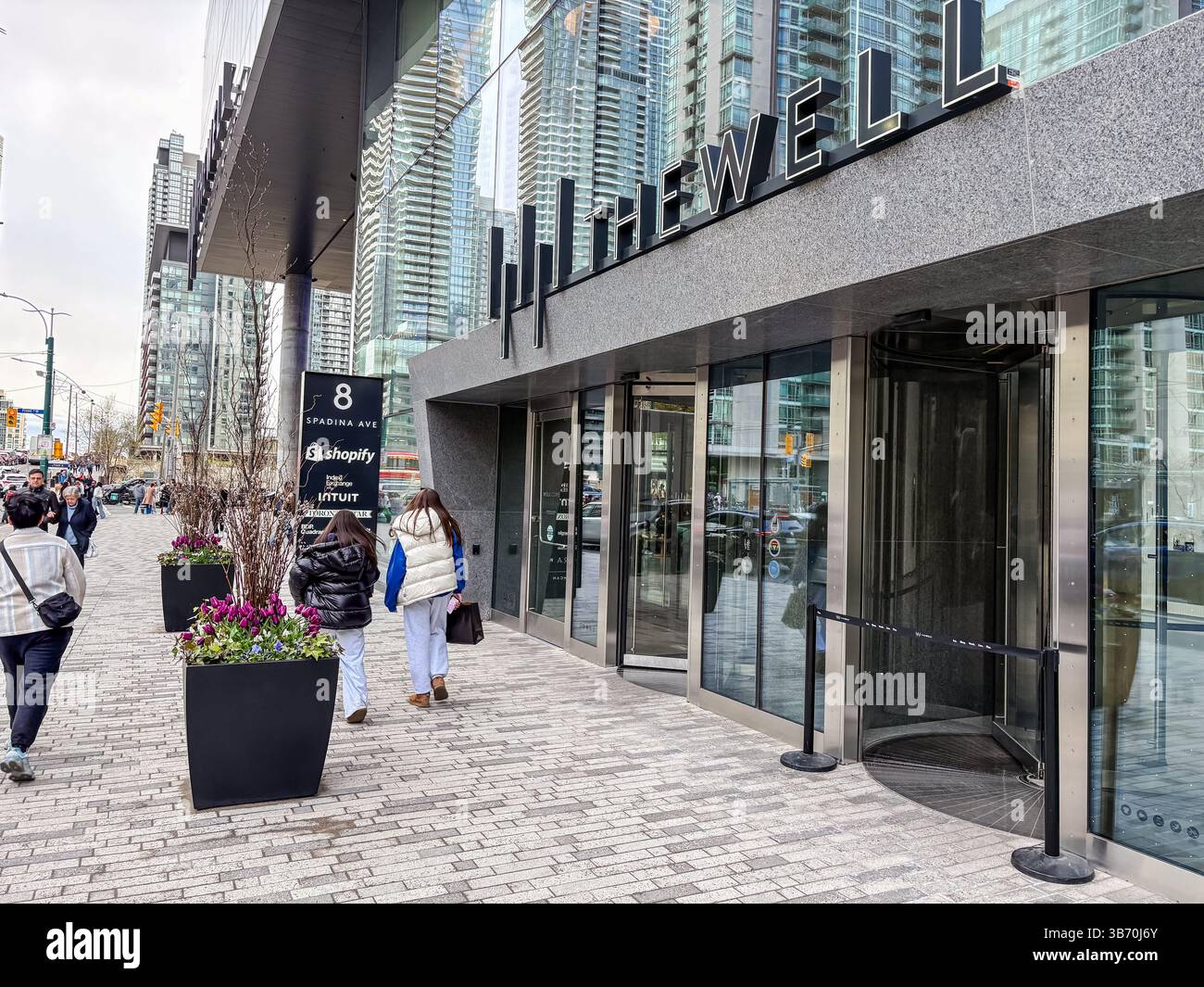 The Well, Toronto, Canada. Modern mixed-use building entrance with glass facade, revolving doors, and street view with people walking. Stock Photo