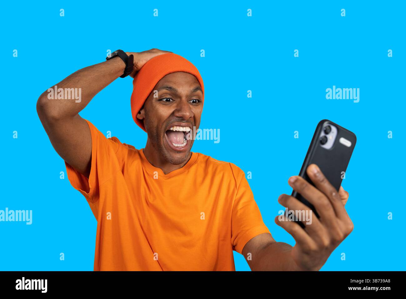 Young man expressing excitement while using smartphone against a vibrant blue backdrop Stock Photo