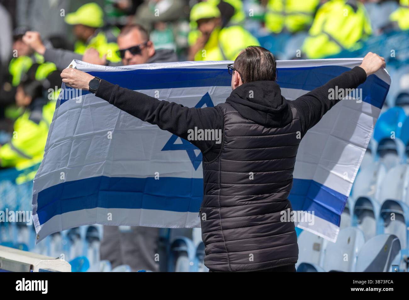 Football fan attending the Rangers v Celtic match at Ibrox stadium, Glasgow, holds up an Israeli flag towards the Celtic supporters Stock Photo