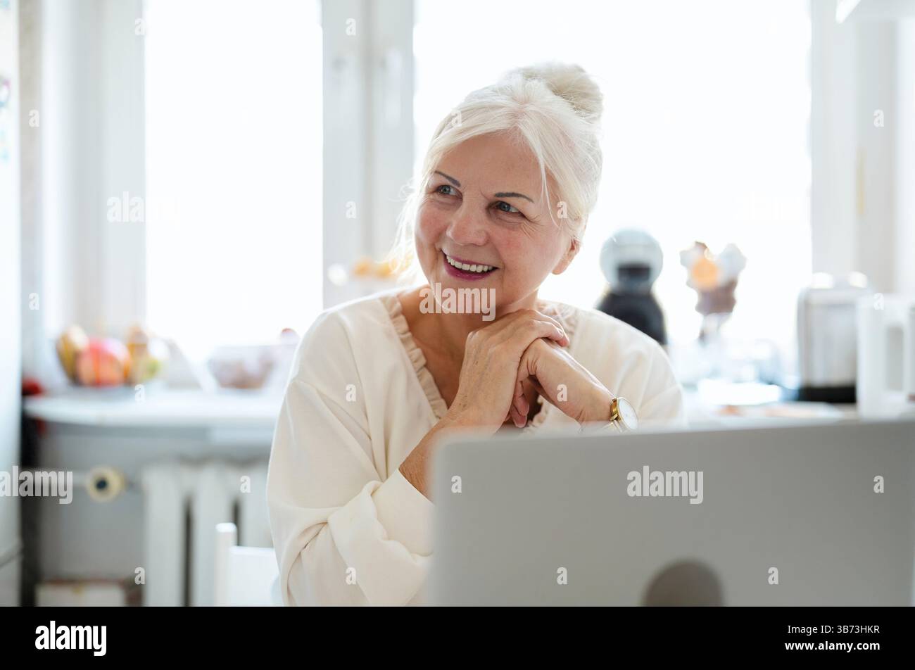 Mature woman working with her laptop at home kitchen Stock Photo