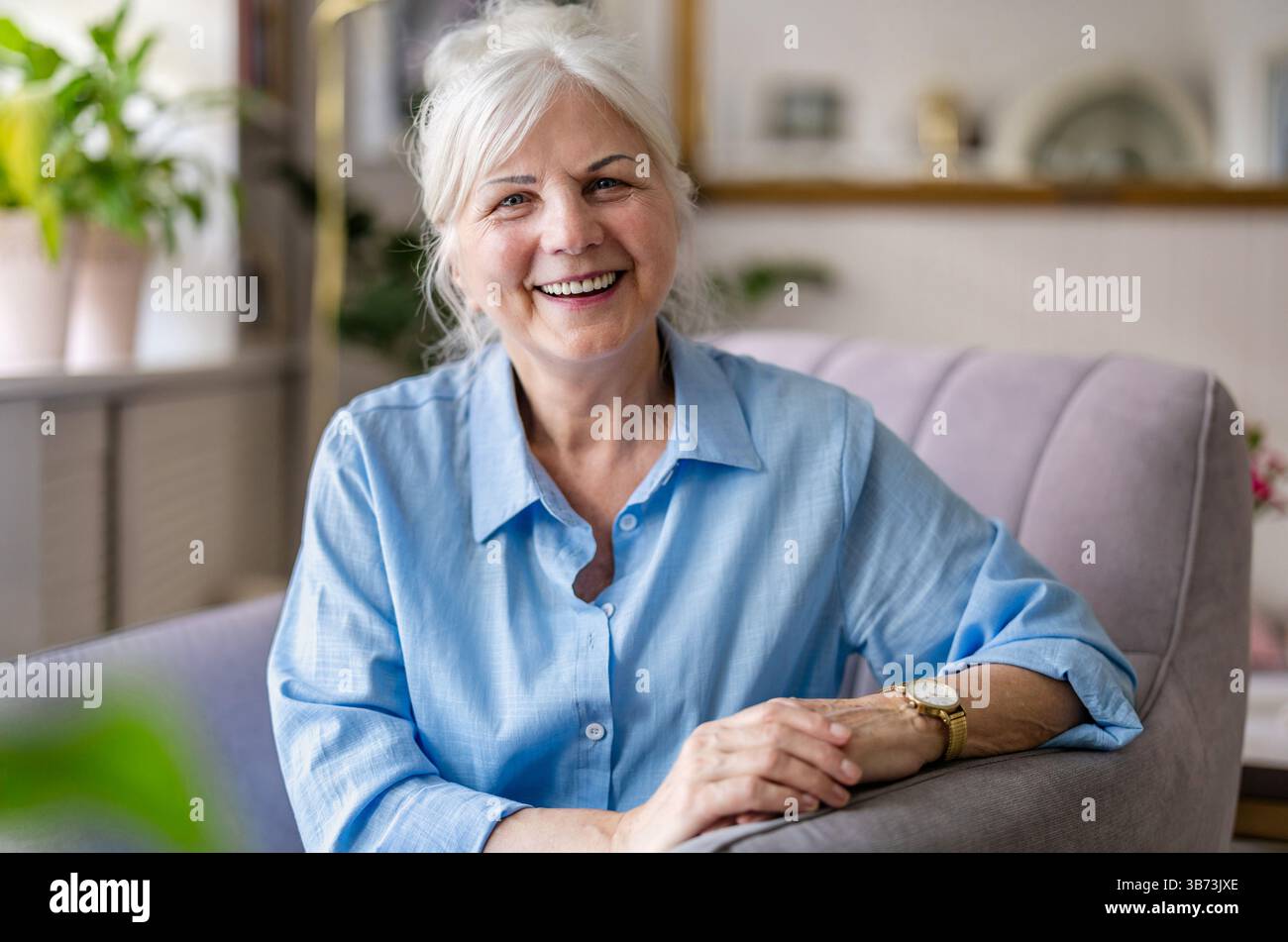 Happy senior woman at home sitting in armchair and looking at camera Stock Photo