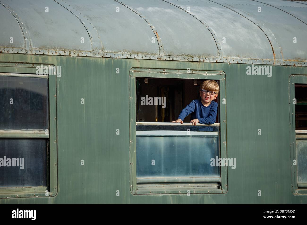 Blond boy leans out train window study rural tracks and fields Stock Photo
