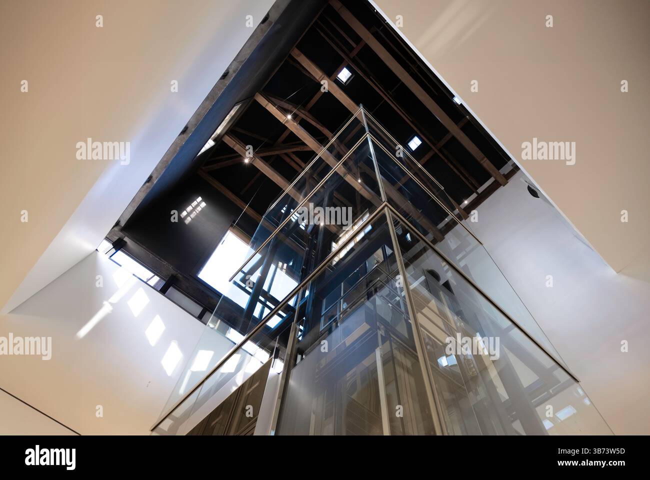 Dramatic shot of a stairwell overlooking an elevator shaft with rods, cables and a glass cabin in a modern building. No people Stock Photo