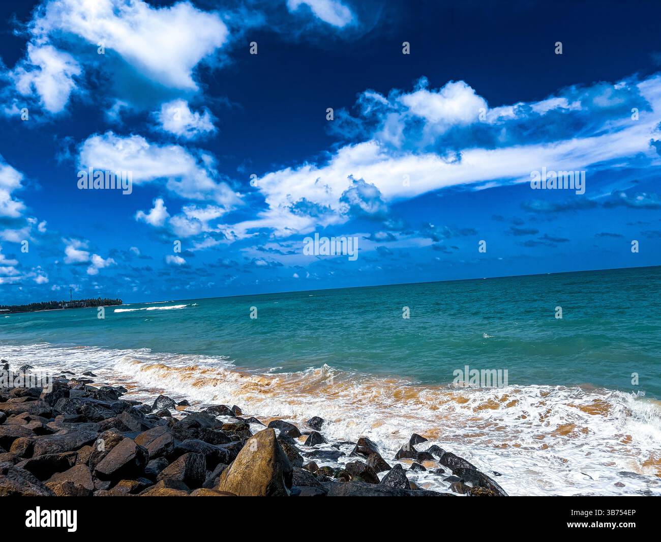 'Scenic coastal view with turquoise ocean waves and a rugged rocky shoreline under a bright blue sky' - Smartphone Captured Stock Image