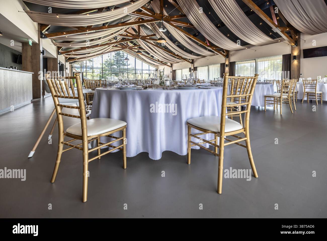 Wedding setting and decorated tables in a beautiful modern interior of a performance hall with a modern light ceiling of wooden construction. Stock Photo