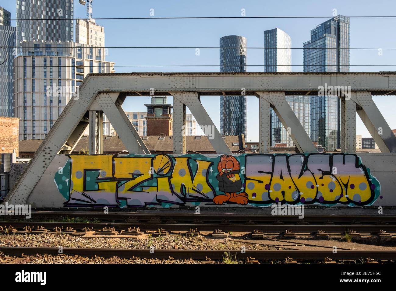 Graffiti on iron train bridge in Manchester with high rise skyscrapers in the background. Northern England, 2025. Stock Photo