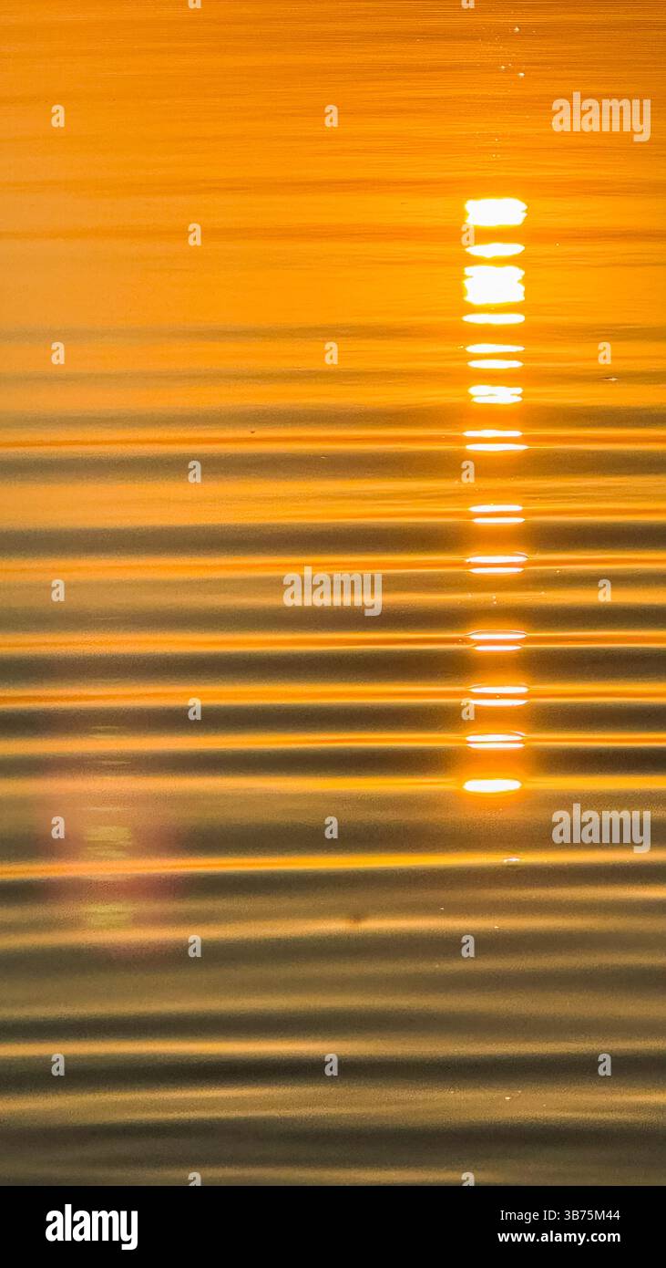 Golden sunset reflection on calm water surface with soft ripples creating a tranquil and serene ambiance capturing nature's beauty. Stock Photo