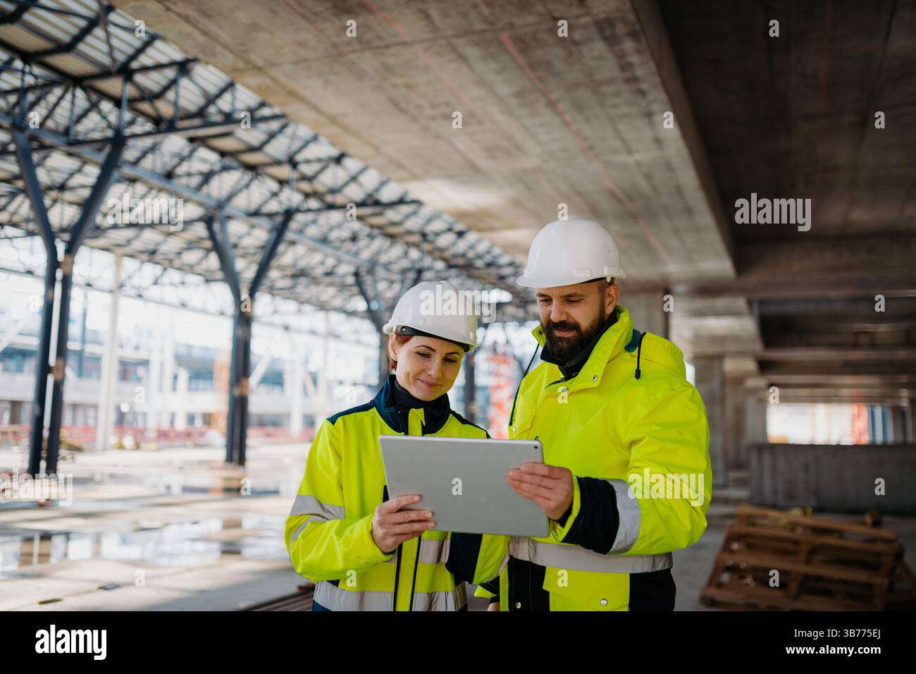Engineers discussing construction plans using a tablet on site. Stock Photo
