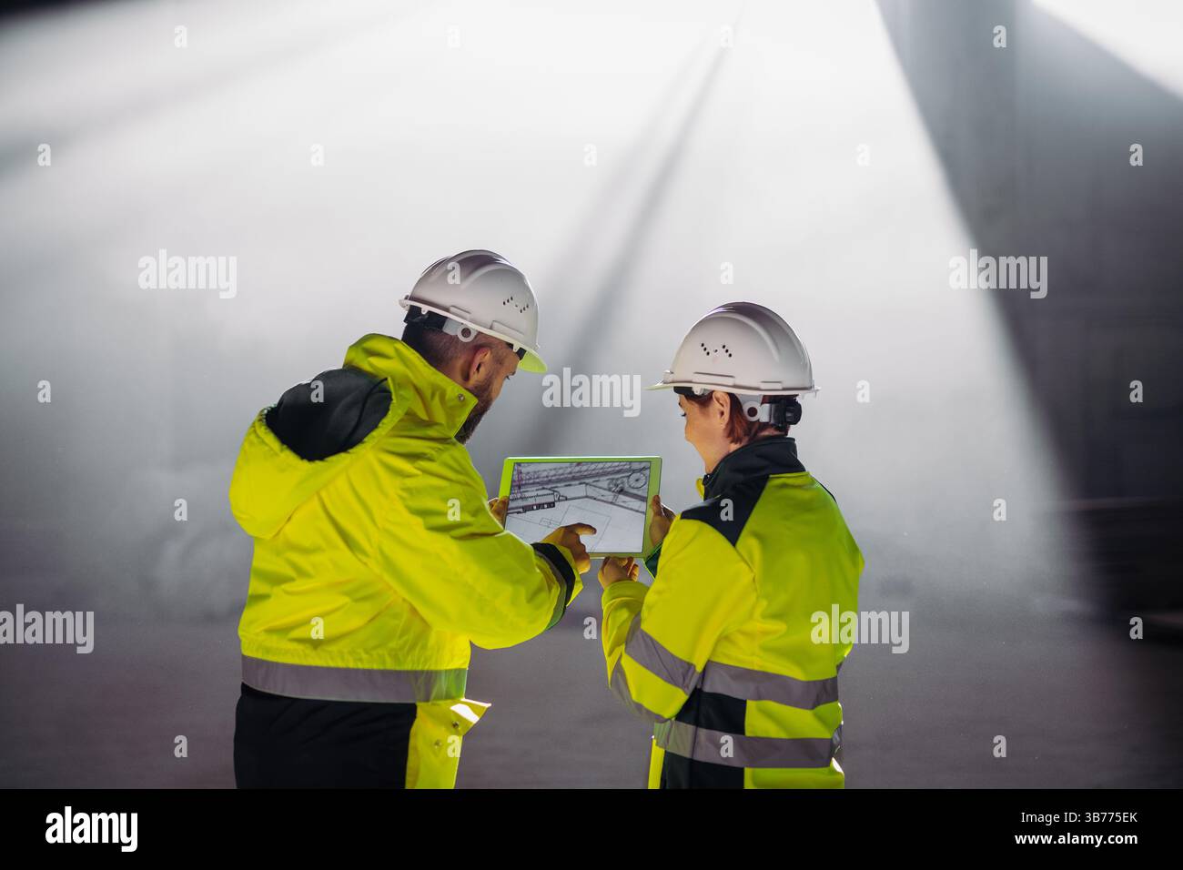 Engineers discussing construction plans using a tablet on site. Stock Photo
