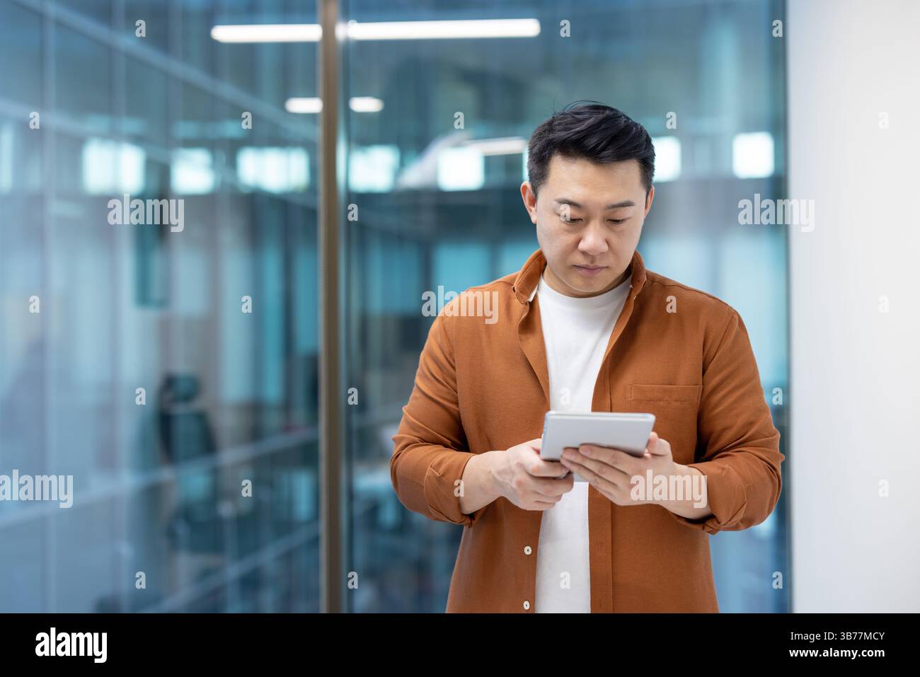 A focused programmer is seen thoughtfully interacting with a tablet device in a modern office setting. Stock Photo