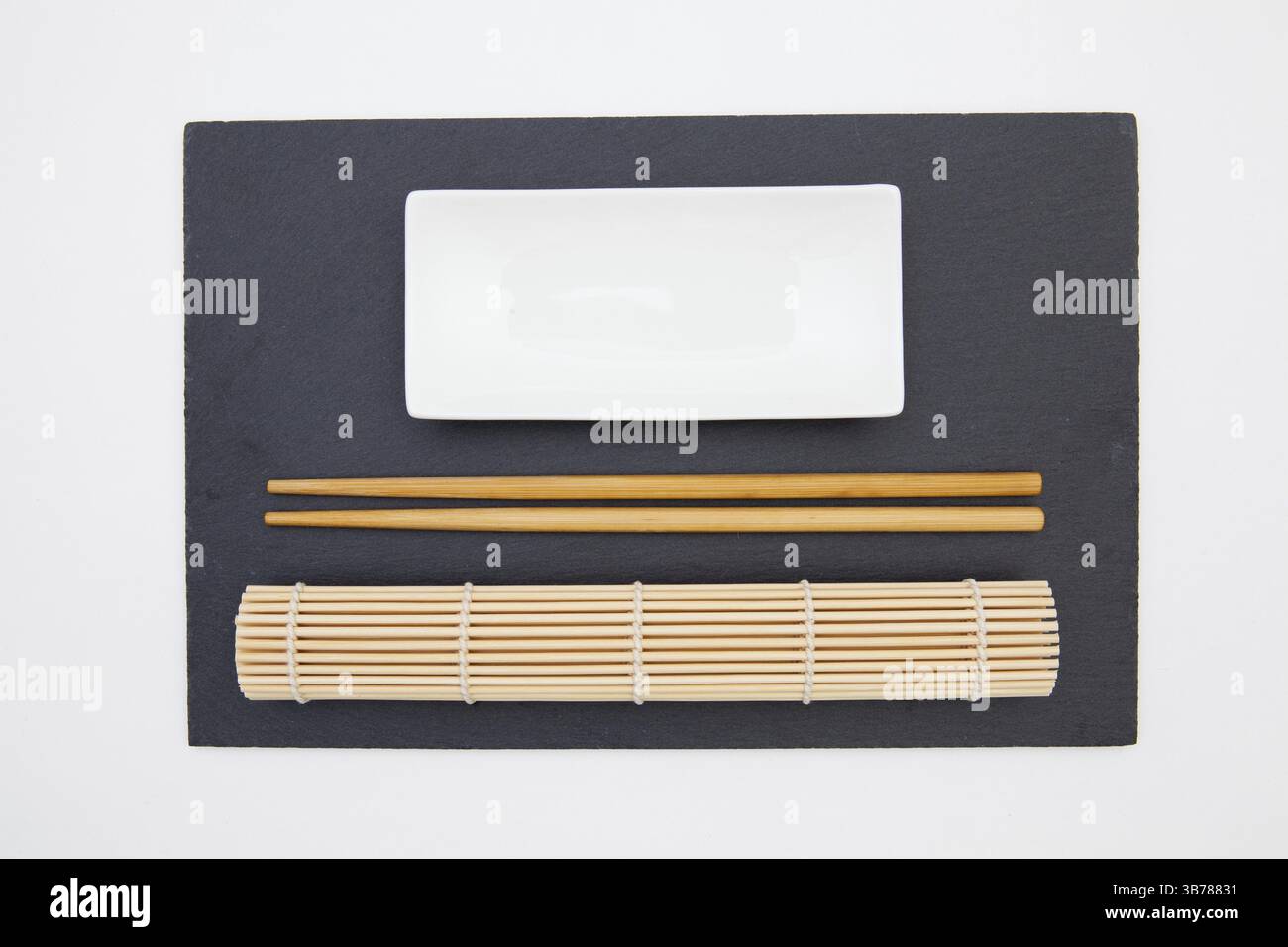 Rectangular slate plate with chopsticks, ceramic plate, bamboo mat for sushi on the white table. Food Design Stock Photo