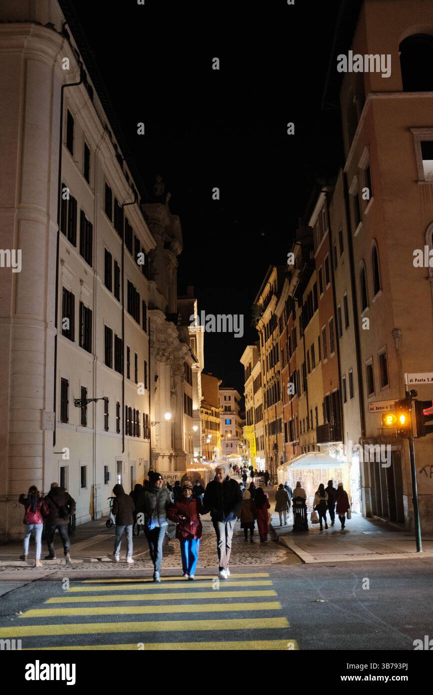 People walking on cobbled streets in central Rome at night under streetlights with Castel Sant Angelo in background and lively atmosphere. High quality photo Stock Photo