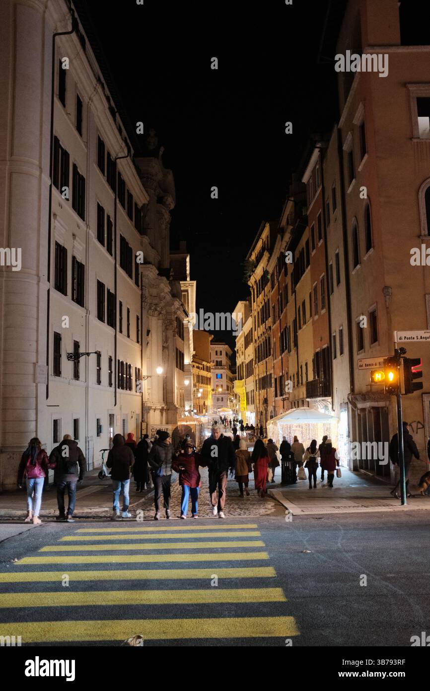 People walking on cobbled streets in central Rome at night under streetlights with Castel Sant Angelo in background and lively atmosphere. High quality photo Stock Photo