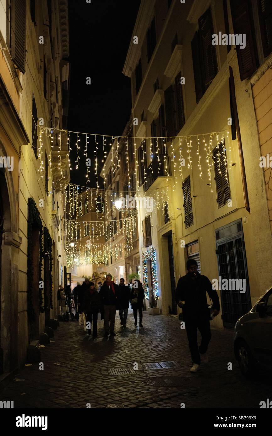Narrow Roman streets decorated with Christmas lights at night people walking and festive atmosphere in old town Italy. High quality photo Stock Photo