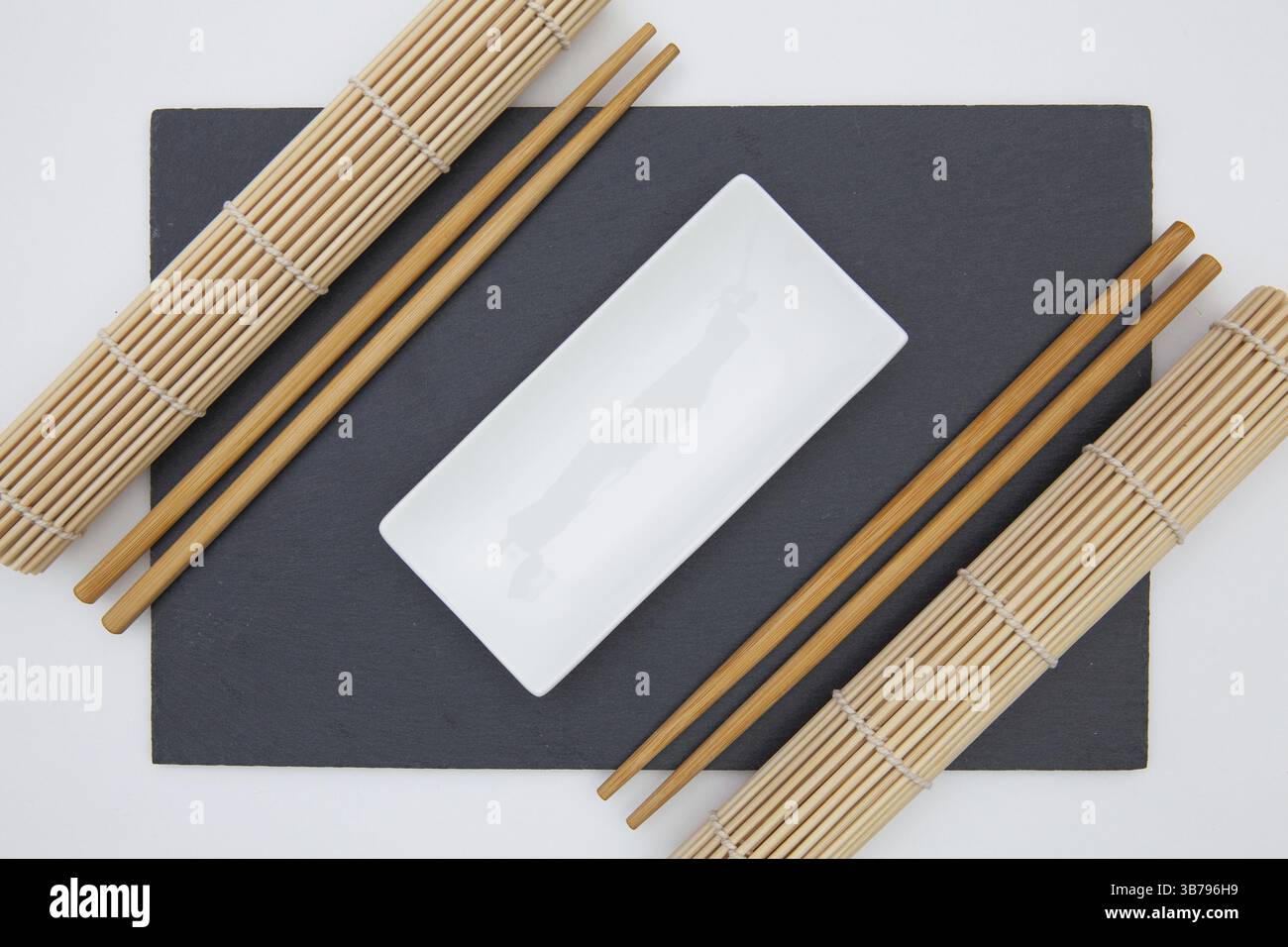 Rectangular slate plate with chopsticks, ceramic plate, bamboo mat for sushi on the white table Stock Photo