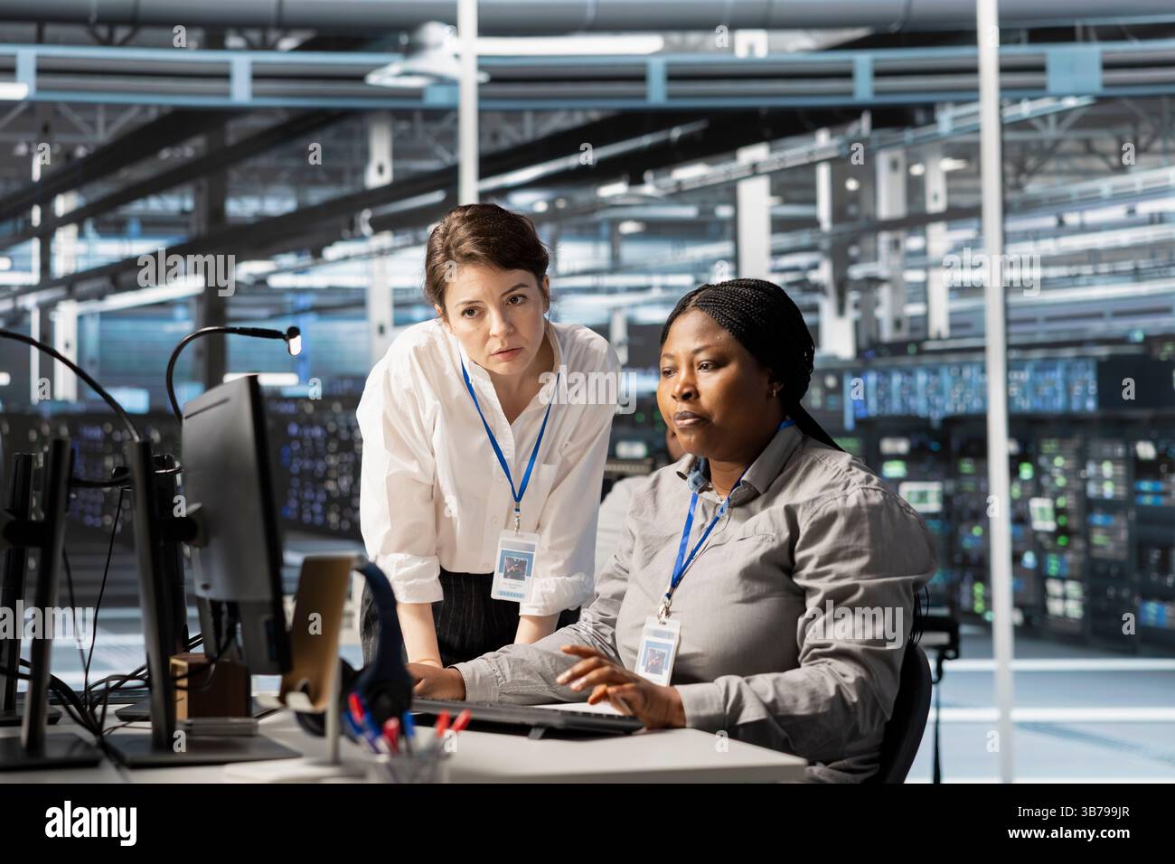 Manager overseeing work done by engineer in server hub, analyzing rigs data. Data center office team leader supervising employee examining supercomputers gear, ensuring system integrity and security Stock Photo