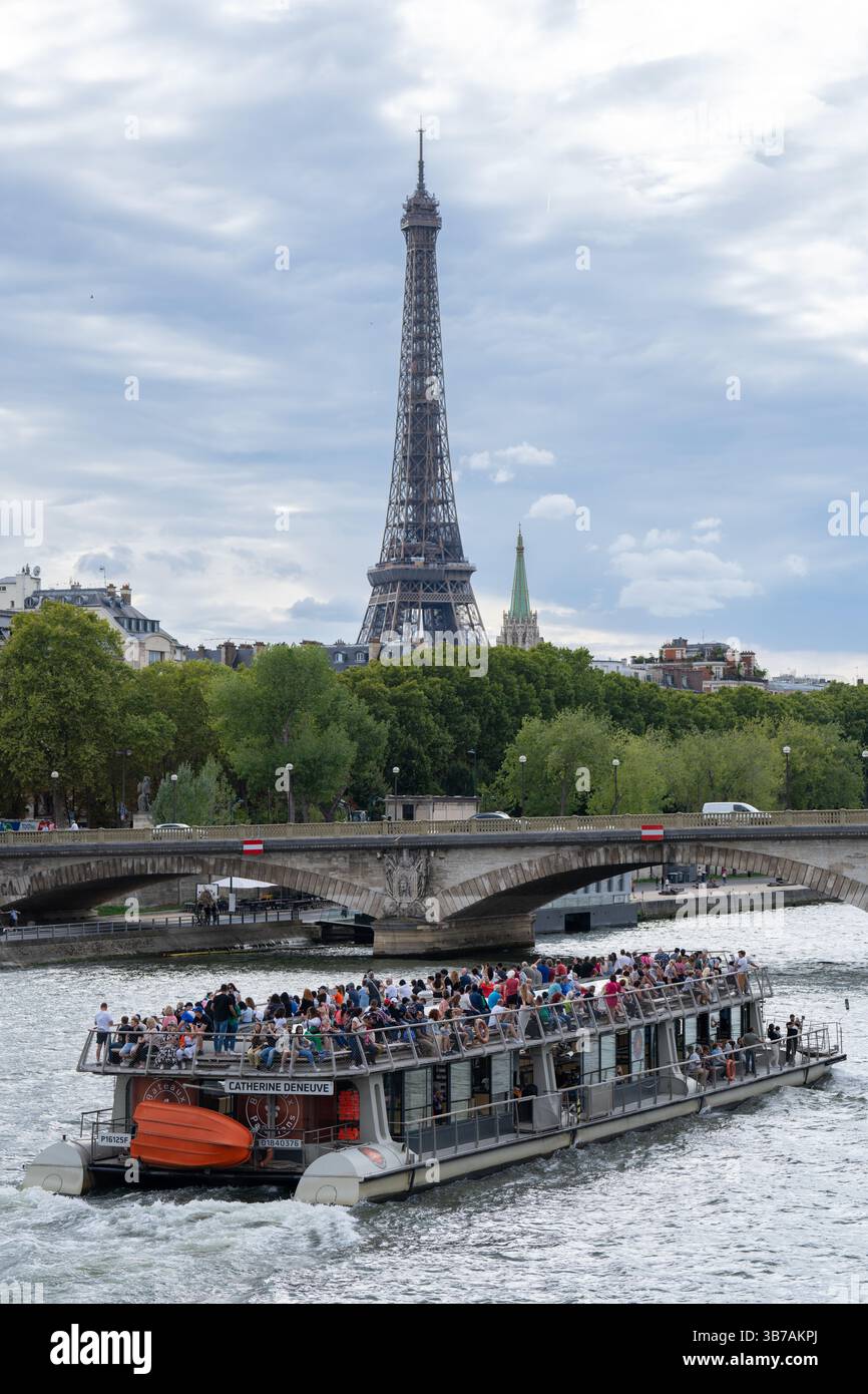 Crowded tourist boat cruising along the Seine River with the Eiffel Tower rising in the background under a cloudy sky in Paris, France Stock Photo