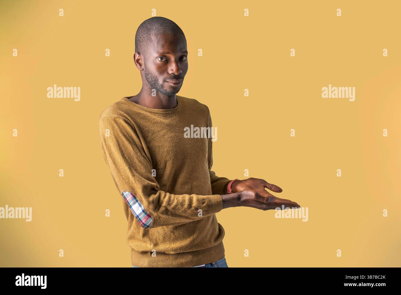 Young black man presenting with empty hands against yellow background, perfect for product mockups Stock Photo