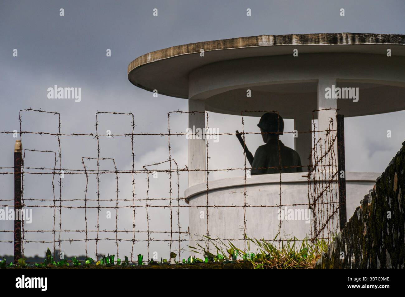 This image shows a guard tower at Con Son Prison, with a barbed wire fence and broken glass along the base for added security. The silhouette of a gua Stock Photo