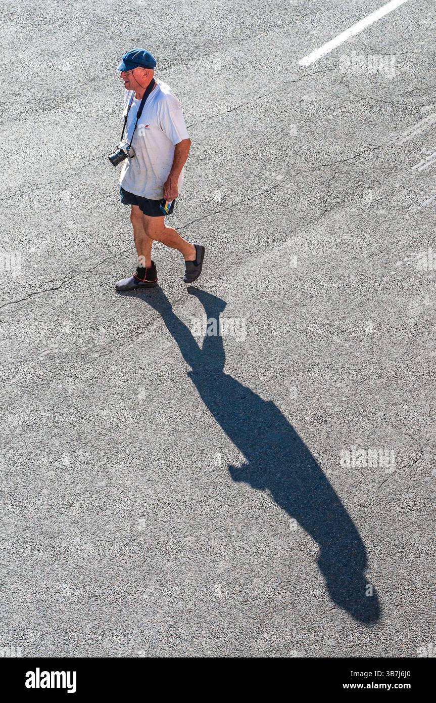 Man with camera walking across street casting a long shadow - Preuilly-sur-Claise, Indre-et-Loire (37), France. Stock Photo