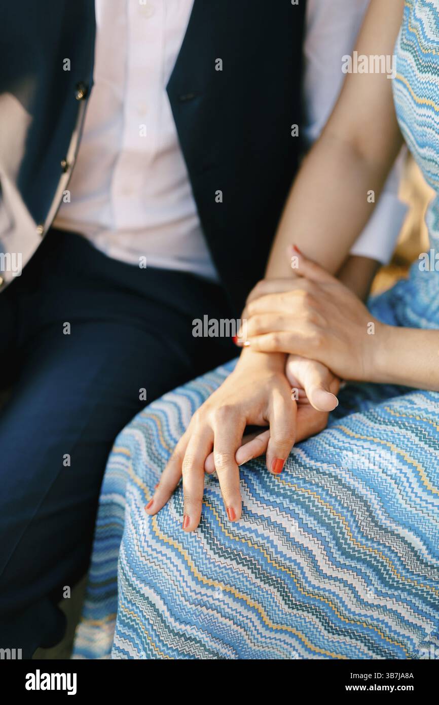 Man in a suit and woman in a striped blue dress are sitting holding ...