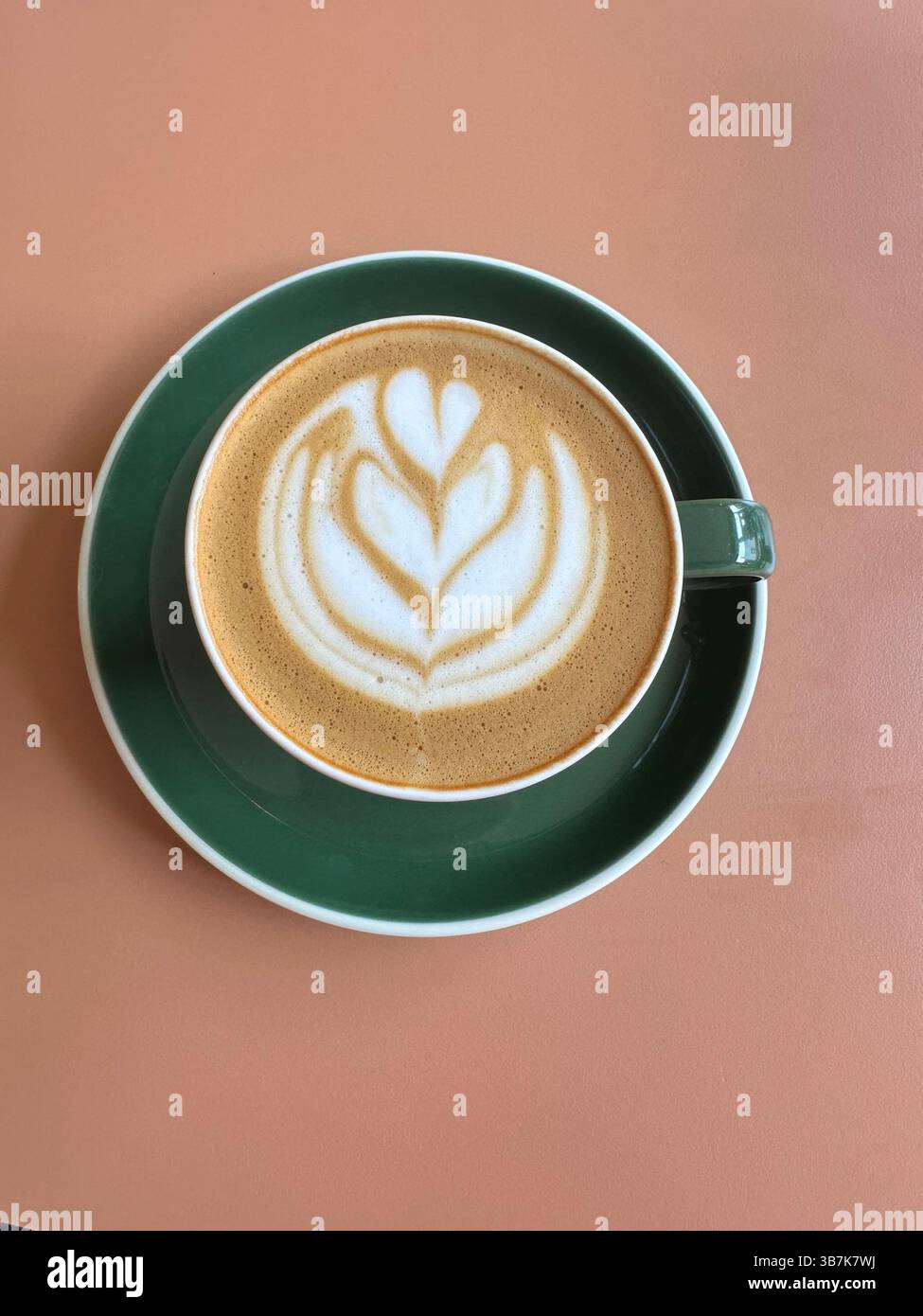 Flat white coffee in green cup and saucer on peach background, overhead view with no spoon. - Smartphone Captured Stock Image