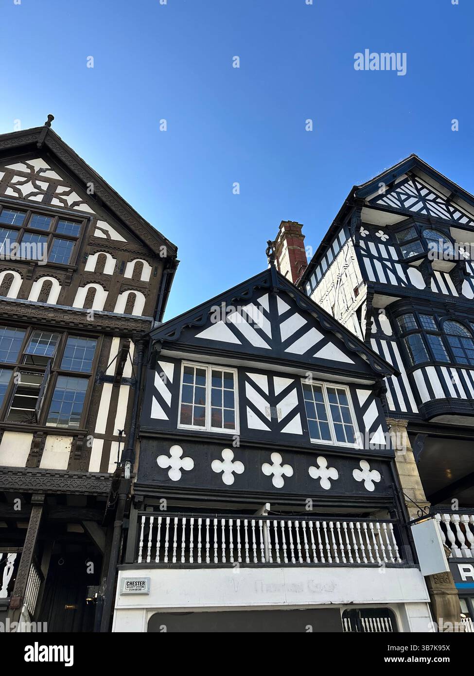 Low-angle view of black and white Tudor-style buildings in Chester, England, against a clear blue sky on a sunny day. - Smartphone Captured Stock Image