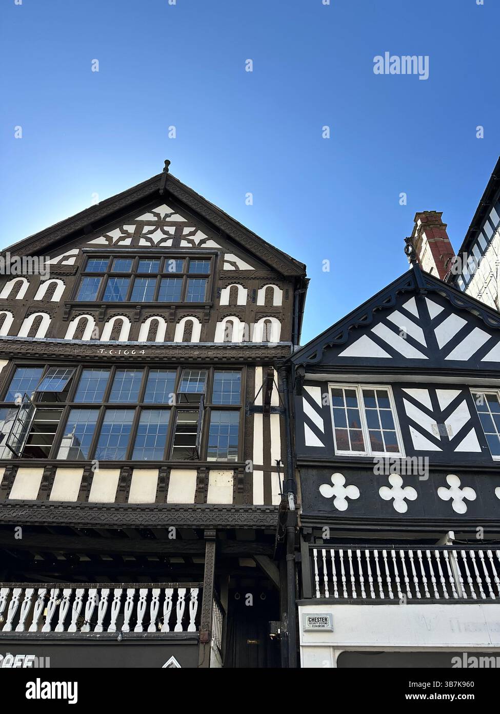 Low-angle view of black and white Tudor-style buildings in Chester, England, against a clear blue sky on a sunny day. - Smartphone Captured Stock Image