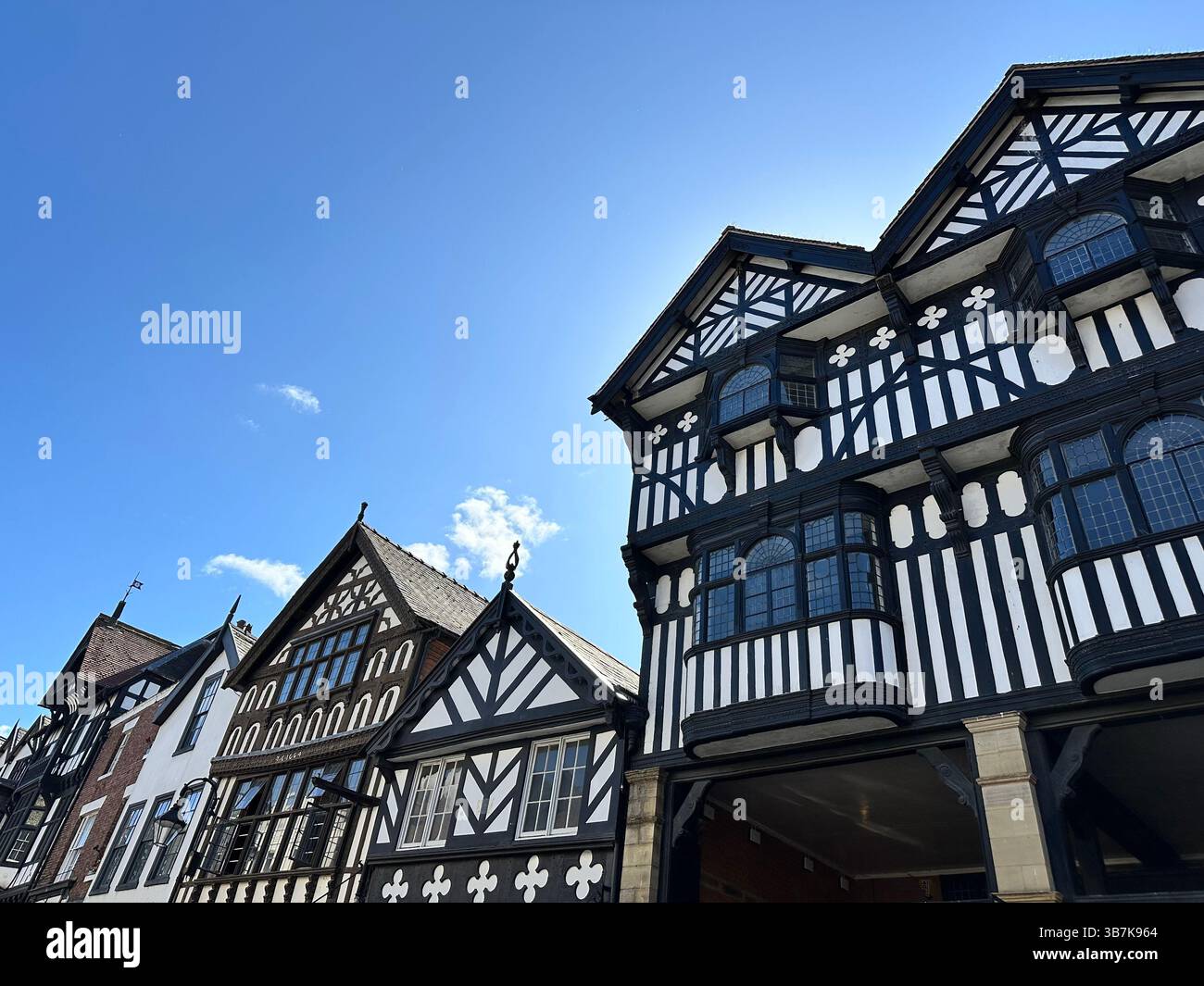 Low-angle view of black and white Tudor-style buildings in Chester, England, against a clear blue sky on a sunny day. - Smartphone Captured Stock Image
