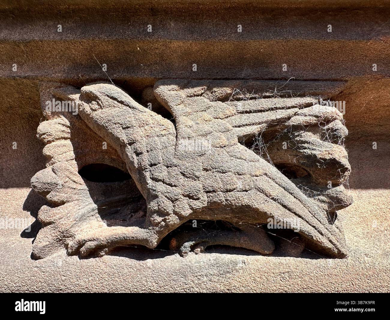 Close up of ornate red brick carvings on Chester Cathedral featuring a bird with visible cobwebs Stock Photo