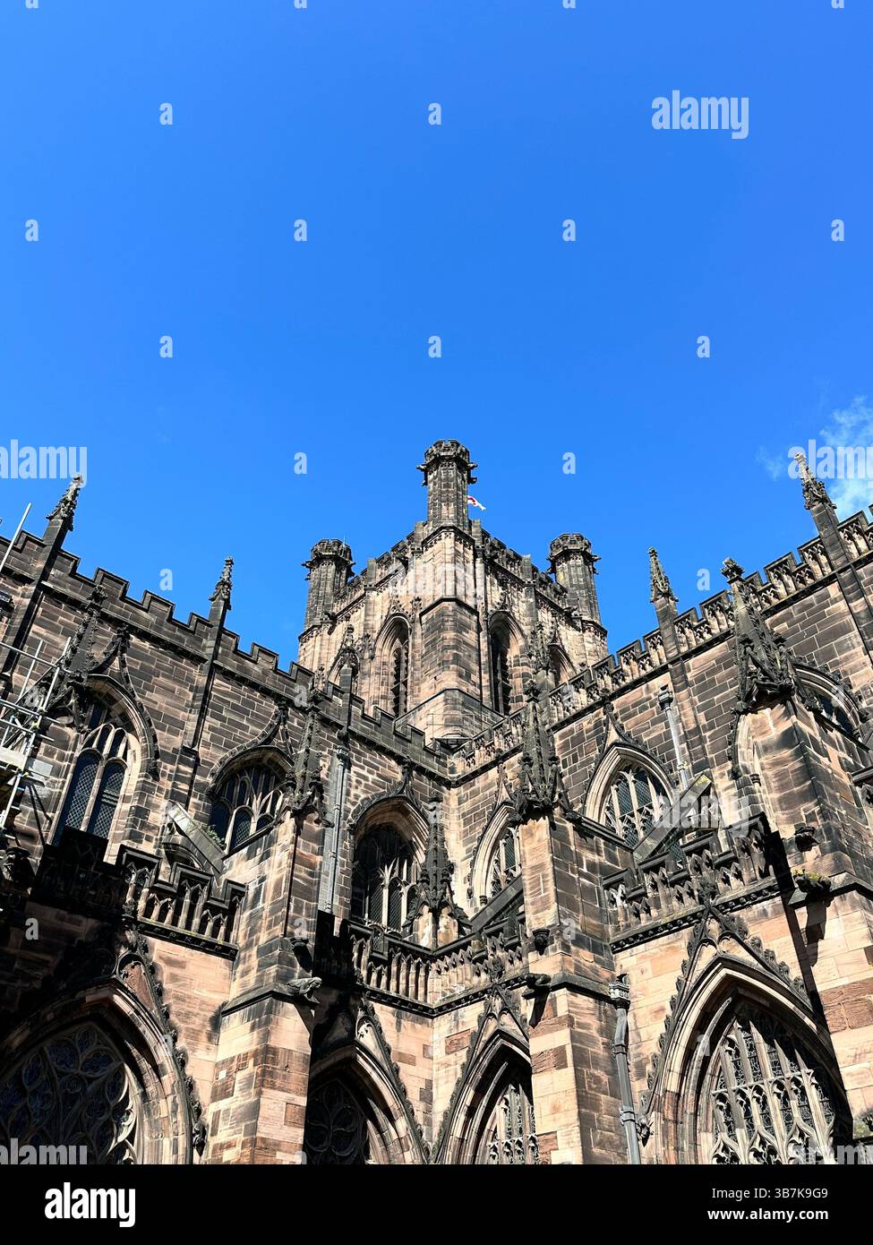 Upward view of Chester Cathedral with red sandstone tower against clear blue sky on a sunny day, capturing historic architecture and contrast - Smartphone Captured Stock Image
